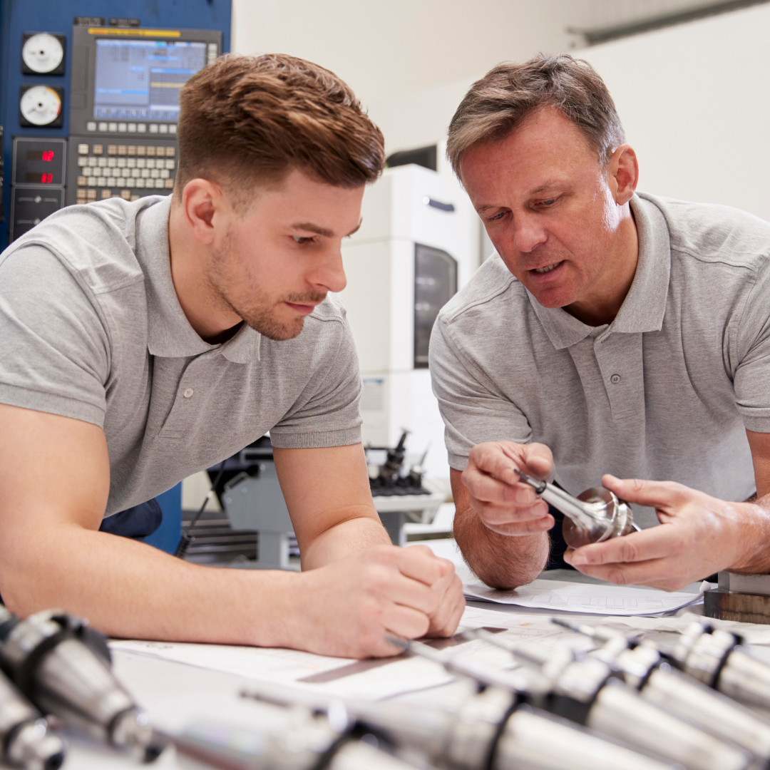 Untitled design (7) Two engineers discussing a machine's component.