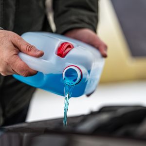 driver refilling the blue non-freezing windshield washer liquid in the tank of the car, closeup driver refilling the blue non-freezing windshield washer liquid in the tank of the car, closeup