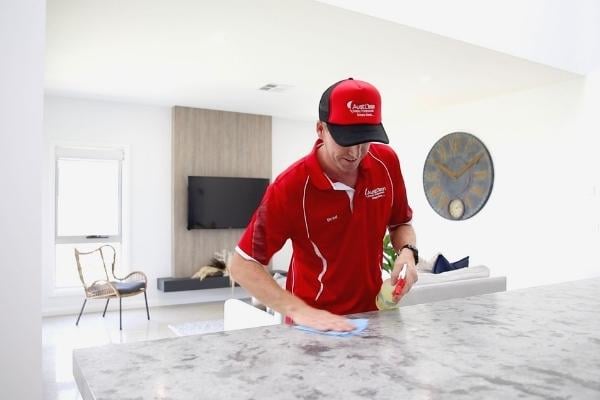 Residential 1 AustClean professional cleaner in red uniform – domestic cleaning service provider cleaning marble countertops in modern Australian home using professional cleaning products and techniques.