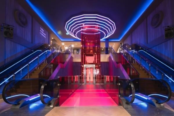 Shopping Centres 2 AustClean shopping centre cleaning – modern, brightly lit lobby with escalators, red glass lift, and blue and pink neon lights, perfectly maintained by professional retail and commercial cleaners in Australia.