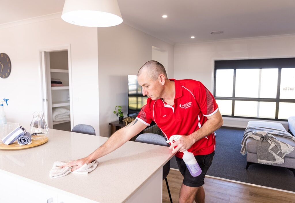 When Should You Book a Professional Spring Clean? 2 AustClean professional cleaner dusting table and furniture surfaces inside a residential home