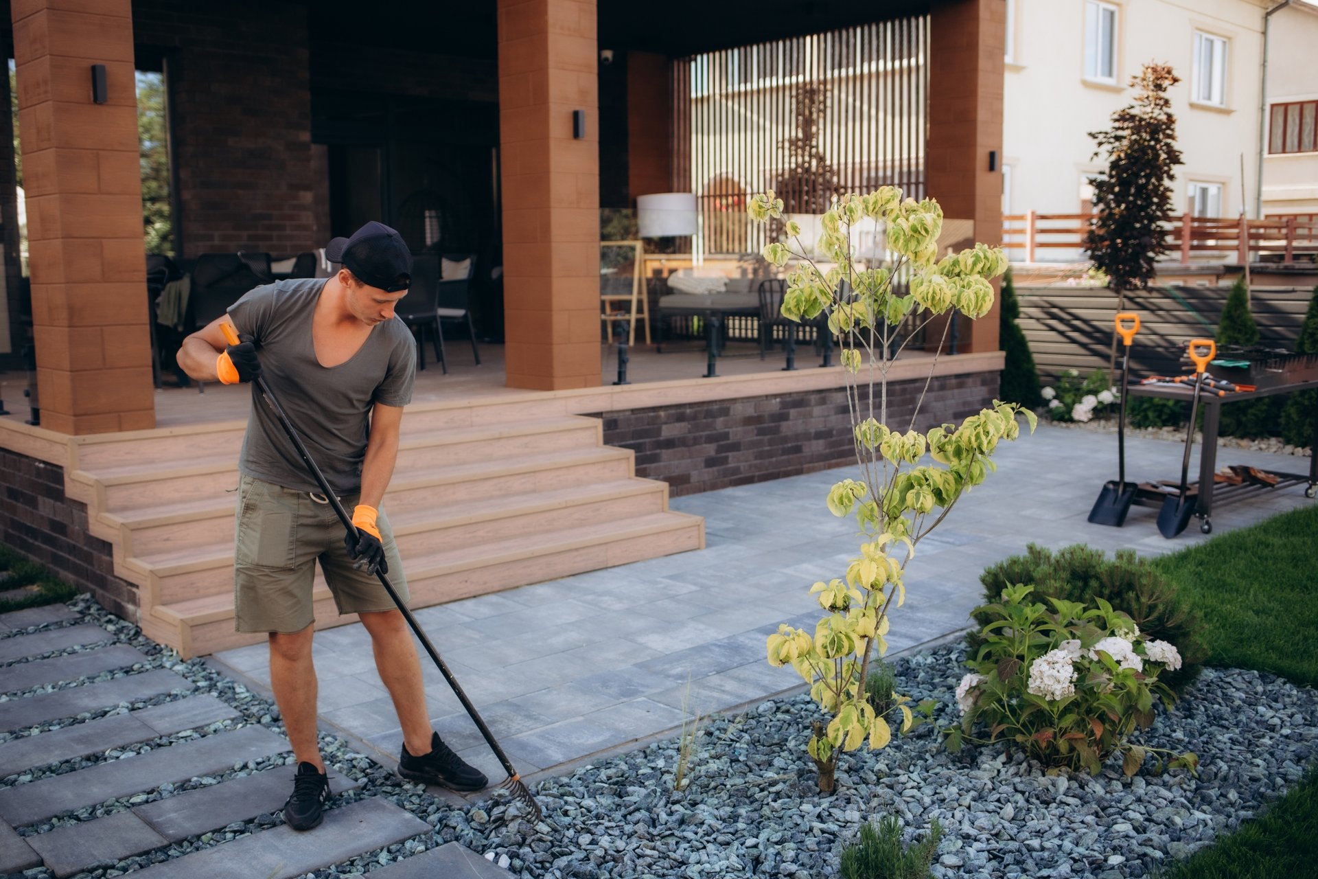Getting Your Adelaide Patio Ready for Summer 1 Person in cap and gloves using rake to groom decorative stones in landscaped garden bed Adelaide SA