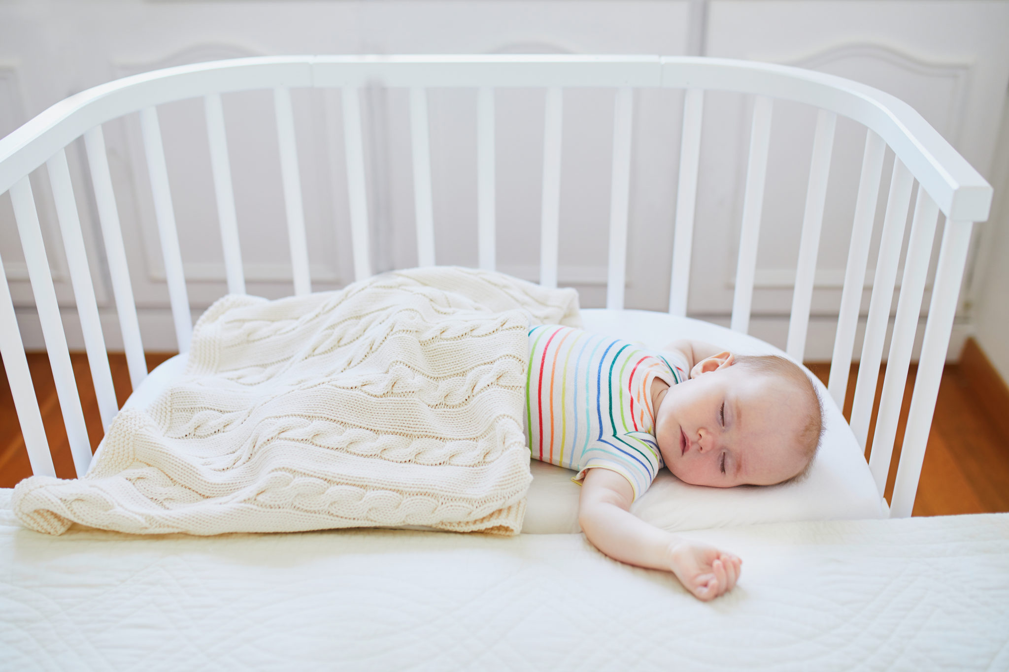 Baby sleeping in co-sleeper crib attached to parents' bed