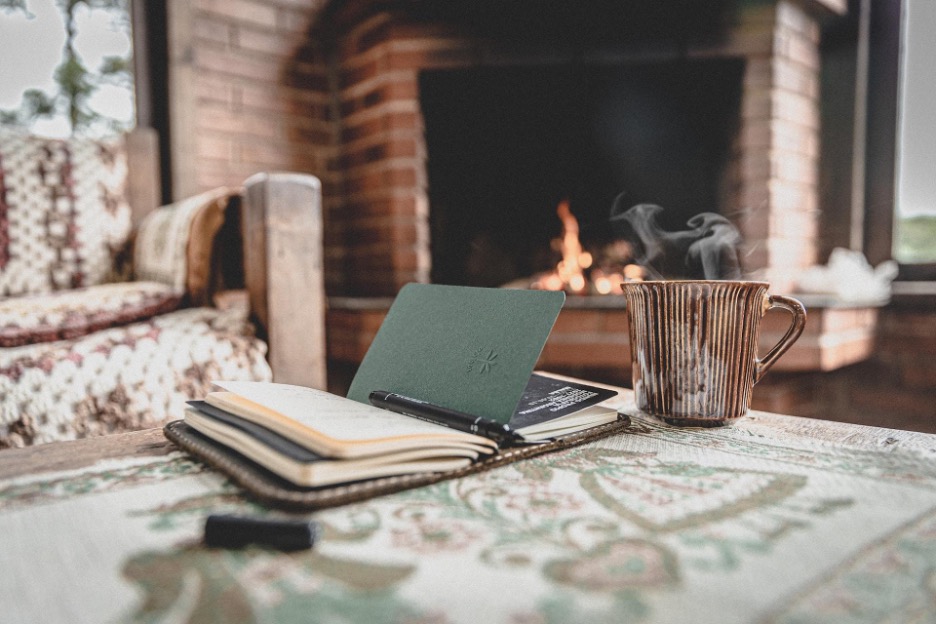 Book with cup of coffee next to it in front of the fireplace.
