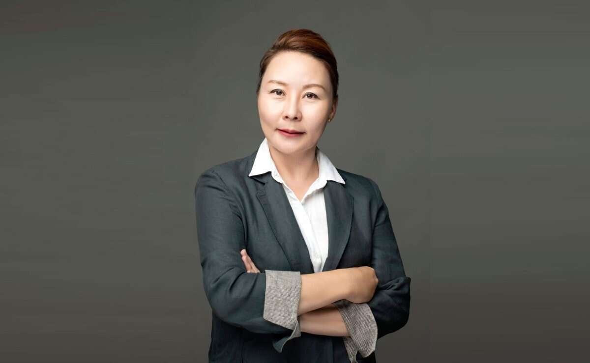 Өөртөө итгэлтэй царайтай эмэгтэй саарал дэвсгэр дээр зогсож байна. Тэрээр цайвар захтай цамцан дээр бараан өнгийн пиджак өмсөж, гараа зөрүүлсэн байна. Түүний үсийг нямбай боож, компаниа удирдахад бэлэн энтрепренерийн тайван байдлыг илтгэнэ. - Business.MN