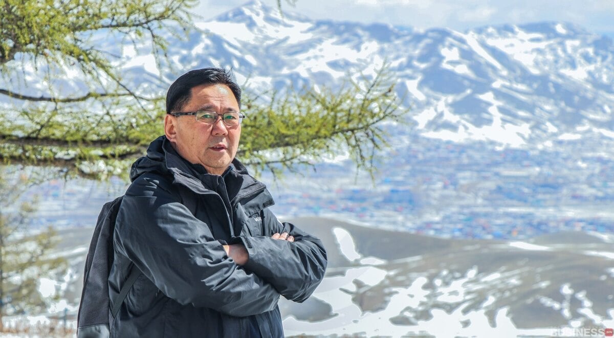 Нүдний шилтэй энтрепренер гадаа цаст уулс, сийрэг модны арын дэвсгэр дээр зогсож байна. - Business.MN