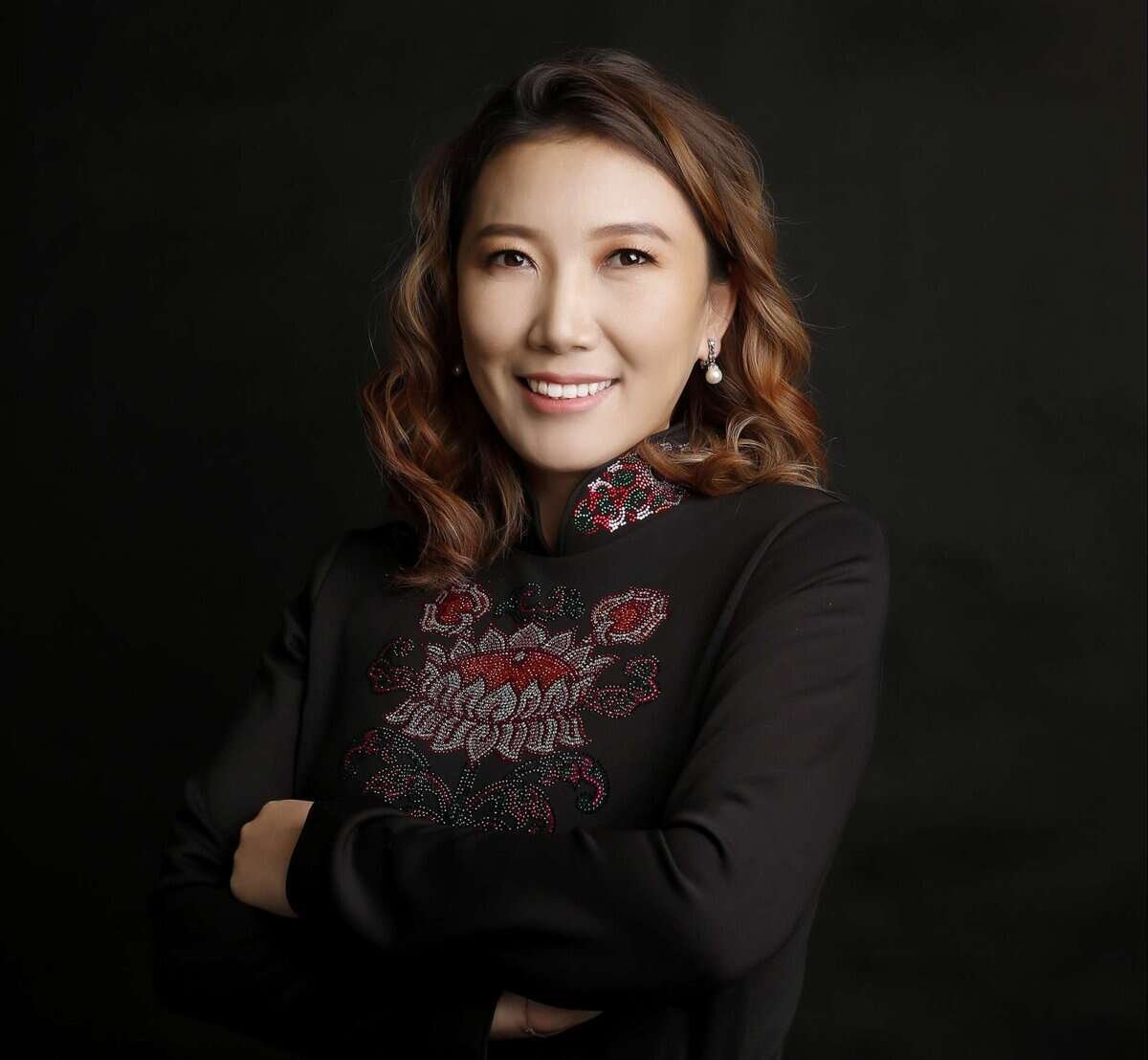 Долгион үстэй эмэгтэй инээмсэглэж, хар хатгамал өмссөн, харанхуй дэвсгэр дээр энтрепренер шиг өөртөө итгэлтэйгээр зурж байна. - Business.MN