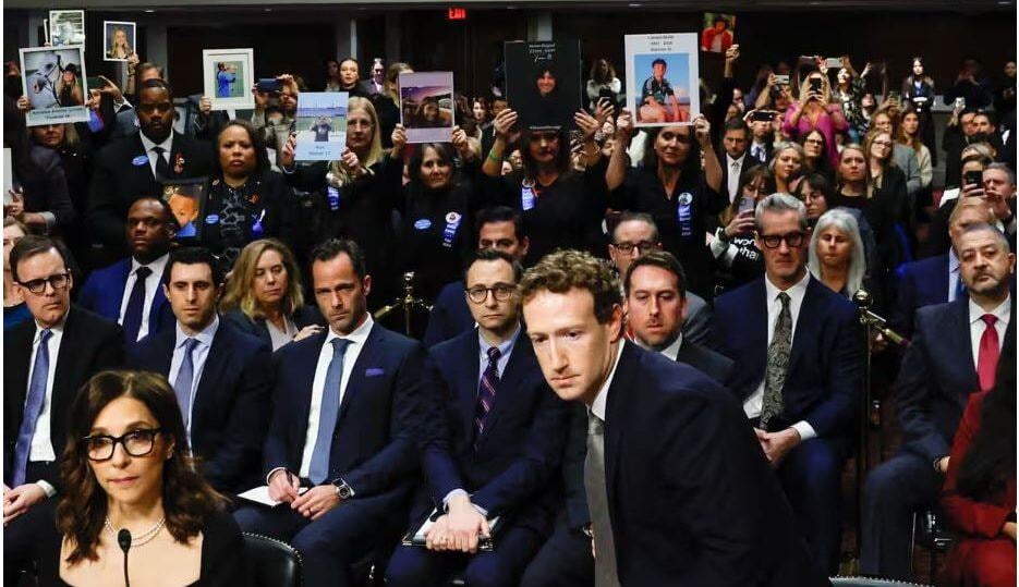 Олон хүн цугларсан шүүхийн танхим албан ёсны хувцас өмссөн хүмүүсээр дүүрэн байна. Урд талд нь костюм өмссөн бизнес эрхэлдэг эрэгтэй суудлаасаа босож байгаа бол нүдний шилтэй эмэгтэй ойролцоо сууж байна. Цаана нь хувь хүмүүс өөр өөр хүмүүсийн зургийг барьж, зарим үзэгчид зураг авдаг. - Business.MN