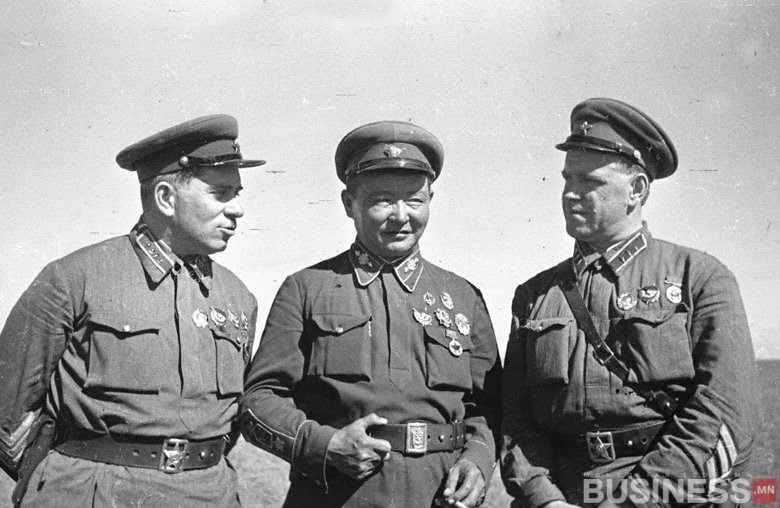 Цэргийн хувцастай гурван эр гадаа инээмсэглэн зогсож байна. Тэд малгай өмсөж, дүрэмт хувцсан дээрээ янз бүрийн медаль, тэмдэгтэй байдаг. Зураг нь хуучин хар цагаан дүр төрхтэй. - Business.MN