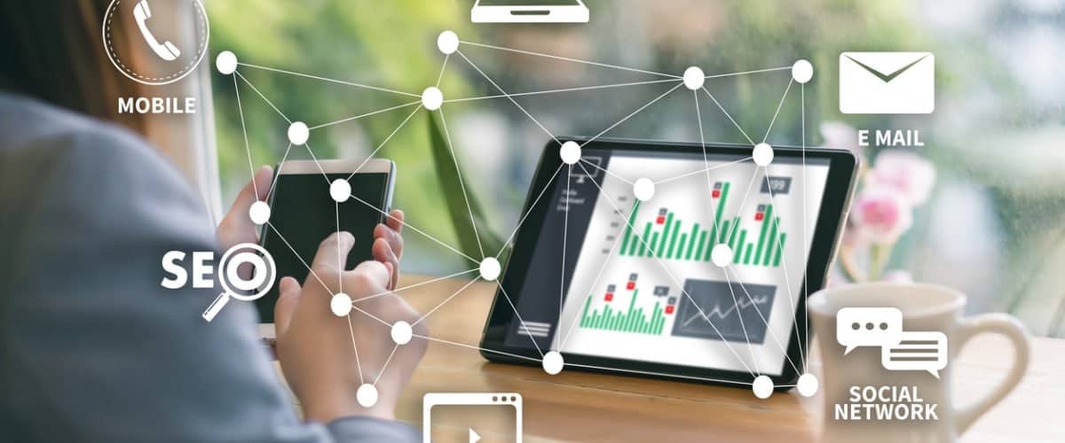 SEO, цахим шуудан, нийгмийн сүлжээ зэрэг хоорондоо холбогдсон дижитал дүрс бүхий ухаалаг утас, зөөврийн компьютер ашигладаг хүн. Зөөврийн компьютер нь график, графикуудыг харуулдаг. Арын дэвсгэр дээр ногоон байгууламжийн бүдэг бадаг харагдаж байна. - Business.MN