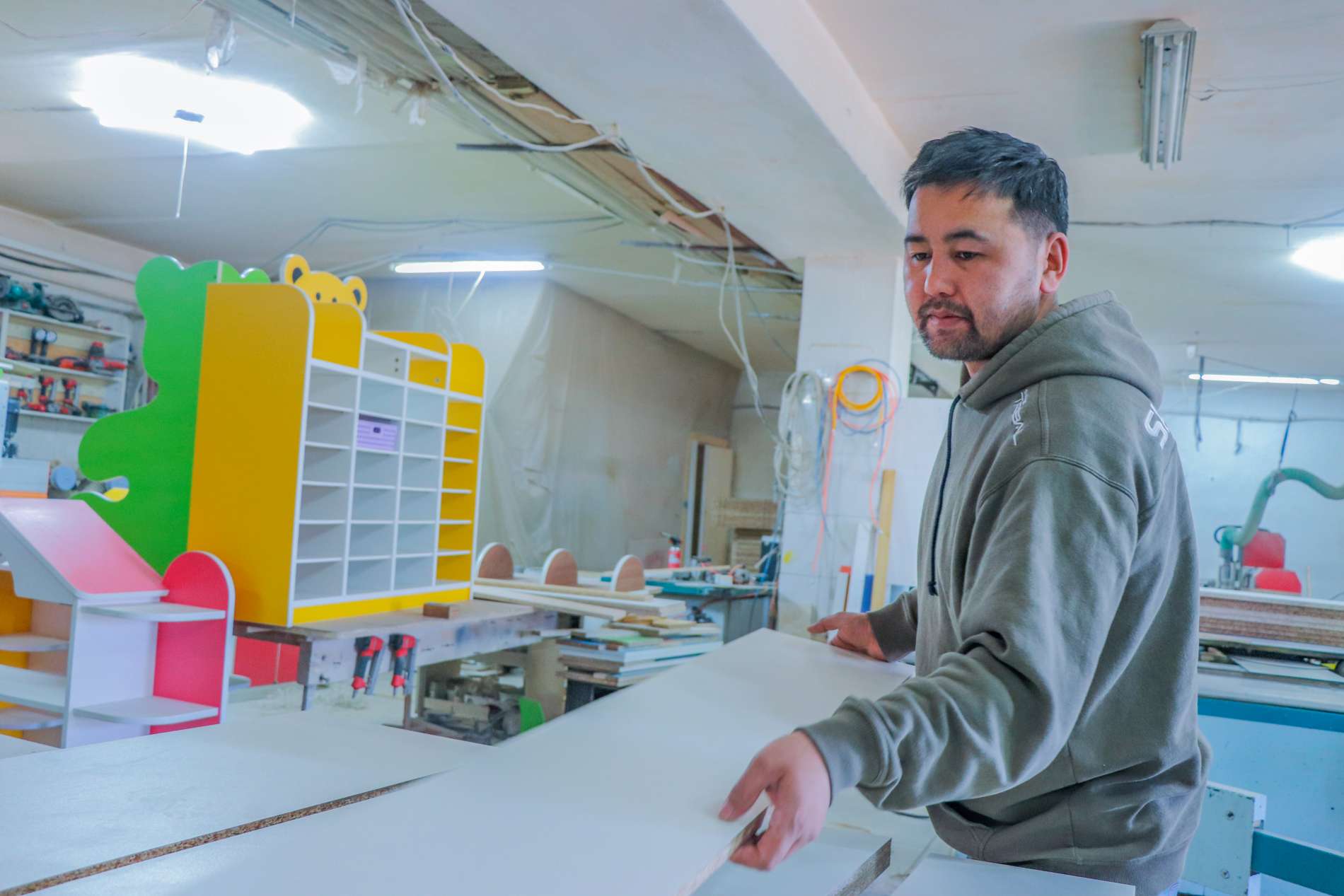 Урланд ажиллаж буй эр, өнгөлөг тавиур, ар талдаа багаж хэрэгсэл бүхий модон эд ангиудыг харьцаж байгаа нь түүний цэцэглэн хөгжиж буй бизнесийн гол цөм болох энтрепренерийн сүнсийг тусгасан. - Business.MN