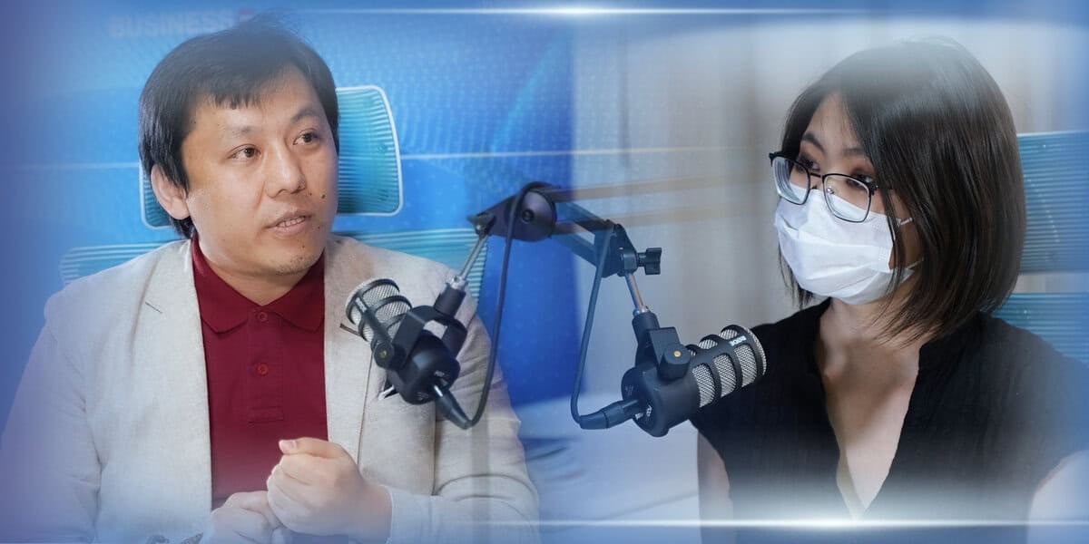 Компанийн стратегийн талаар ярилцаж эсвэл энтрепренерийн ойлголтоо хуваалцаж магадгүй хоёр хүн студийн тохиргоонд микрофоноор ярьж байна. Зүүн талд байгаа эрэгтэй шаргал пиджак, улаан цамц өмссөн бол баруун талд байгаа эмэгтэй хар цамц, нүдний шил зүүсэн нүүрний маск зүүсэн байна. Арын дэвсгэр нь цэнхэр өнгийн градиент юм. - Business.MN