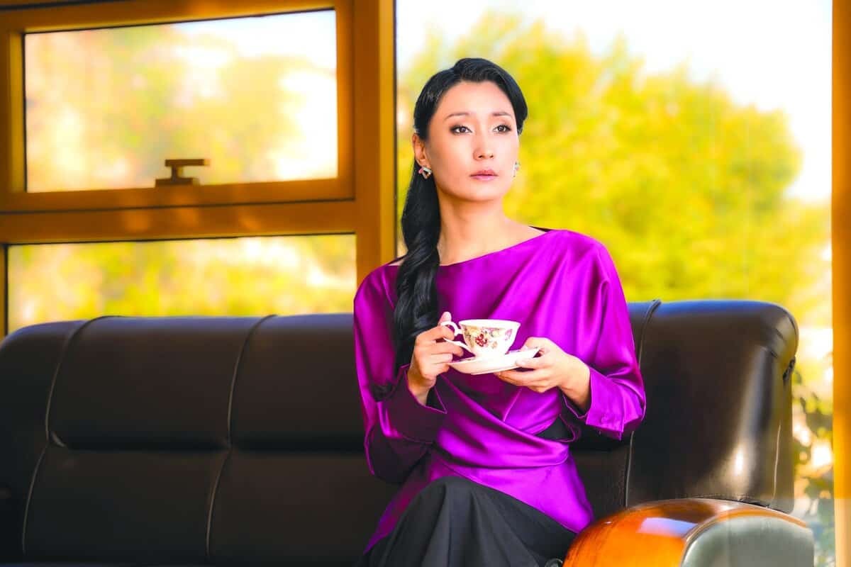 Амт урлаач урласан амт шиг ягаан өнгийн цамц өмссөн эмэгтэй буйдан дээр цайны аяга барин сууна. Тэр цонх руугаа бодолтой ширтэх бөгөөд гадаа байгаа ногоон, намуухан бүдэгхэн харагдах байдал нь нам гүм төрхийг бүрдүүлдэг. - Business.MN