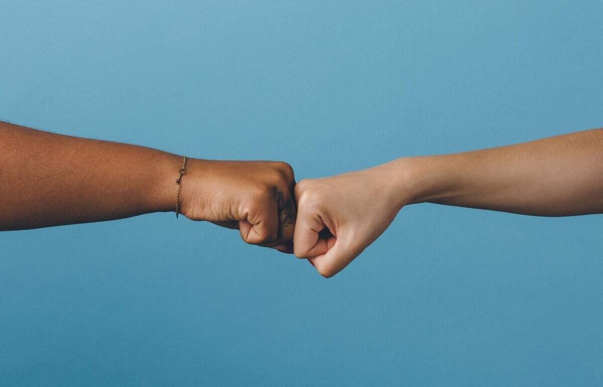 Цэнхэр дэвсгэр дээр нударгаа цохиж буй нэг нь бараан, нөгөө нь цайвар арьстай хоёр хүн. Энэ үзэгдэл нь бизнесийн түншүүд эсвэл энтрепренерүүдийн нийтлэг нөхөрлөлийг илэрхийлдэг. Зүүн талд байгаа хүн бугуйвч зүүдэг. Хоёр гар нь хүрээний төвд хэвтээ байрлалтай байна. - Business.MN