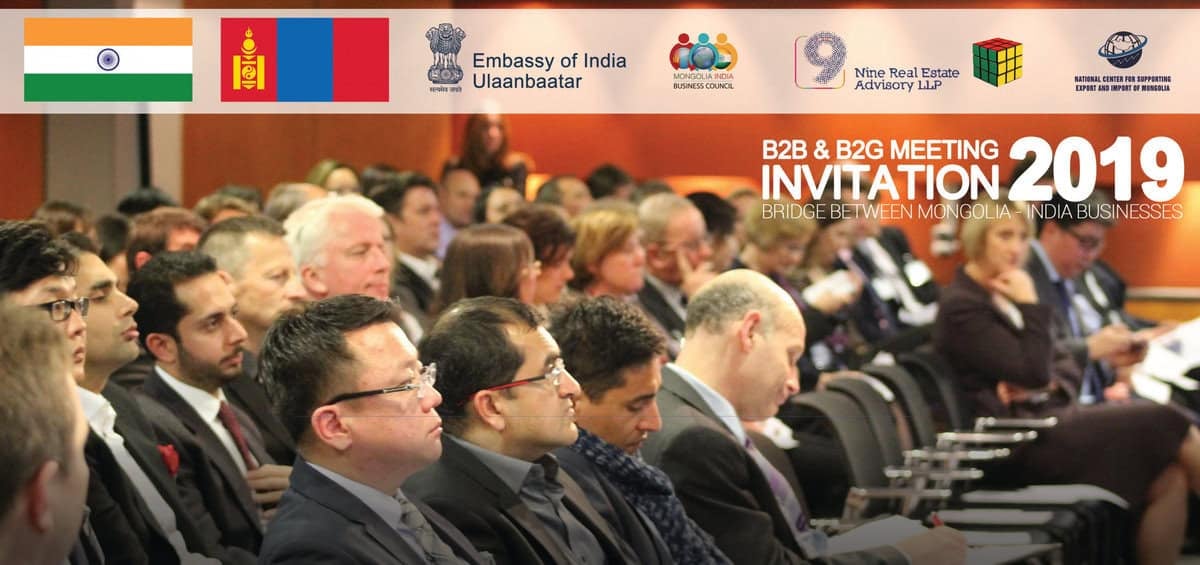 Бизнес уулзалтанд сууж буй үзэгчид анхааралтай сонсож байна. Энэхүү арга хэмжээ нь "B2B & B2G уулзалтын урилга 2019" нэртэй бөгөөд Энэтхэг-Монголын бизнесийн хамтын ажиллагаанд чиглэж байна. Энэтхэг, Монгол улсын төрийн далбаа, арга хэмжээний логоны хамт дээр байрлуулсан байна. - Business.MN