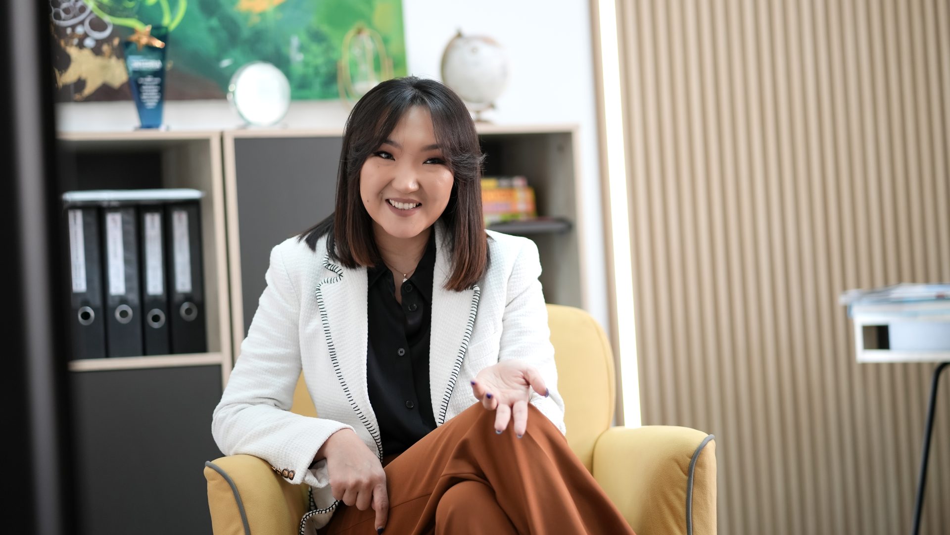 Мөр хүртлээ үстэй хүн шар сандал дээр суугаад инээмсэглэн, нэг гараараа дохино. Тэд хар цамц, бор өмд дээр цагаан пиджак өмссөн байна. Арын дэвсгэр дээр хавтас, ном, бөмбөрцөг, хийсвэр урлаг бүхий номын тавиур байрлуулсан нь тэдний компанийг шинэ өндөрлөгт хөтлөхөд бэлэн, урам зоригтой энтрепренер юм. - Business.MN