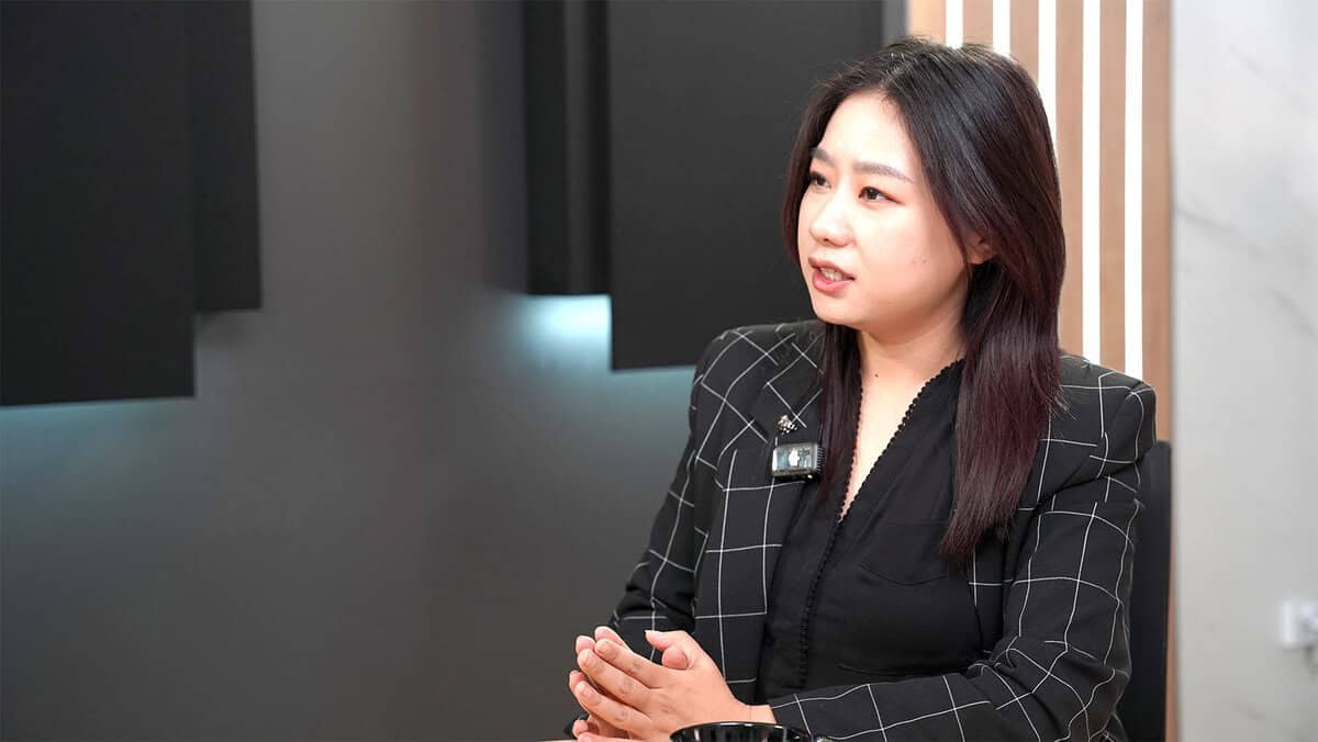 Урт хар үстэй эмэгтэй хар алаг пиджак өмсөж, дотор нь сууж байна. Гараа атгасан яриа өрнүүлж буй тэрээр орчин үеийн дэвсгэр дээр зөөлөн гэрэлтүүлэгтэй, бодит дүрийг дүрсэлжээ. - Business.MN