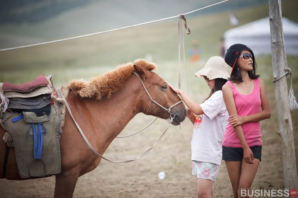 Хөдөө орон нутагт бор морины дэргэд хоёр хүн зогсоно. Нэг нь өргөн захтай малгай, богино өмд өмсөж, морины толгойд зөөлөн хүрдэг. Нөгөөх нь нарны шил зүүж, шон налан сууна. Морин дээр эмээл, цаана нь майхан харагдана. - Business.MN