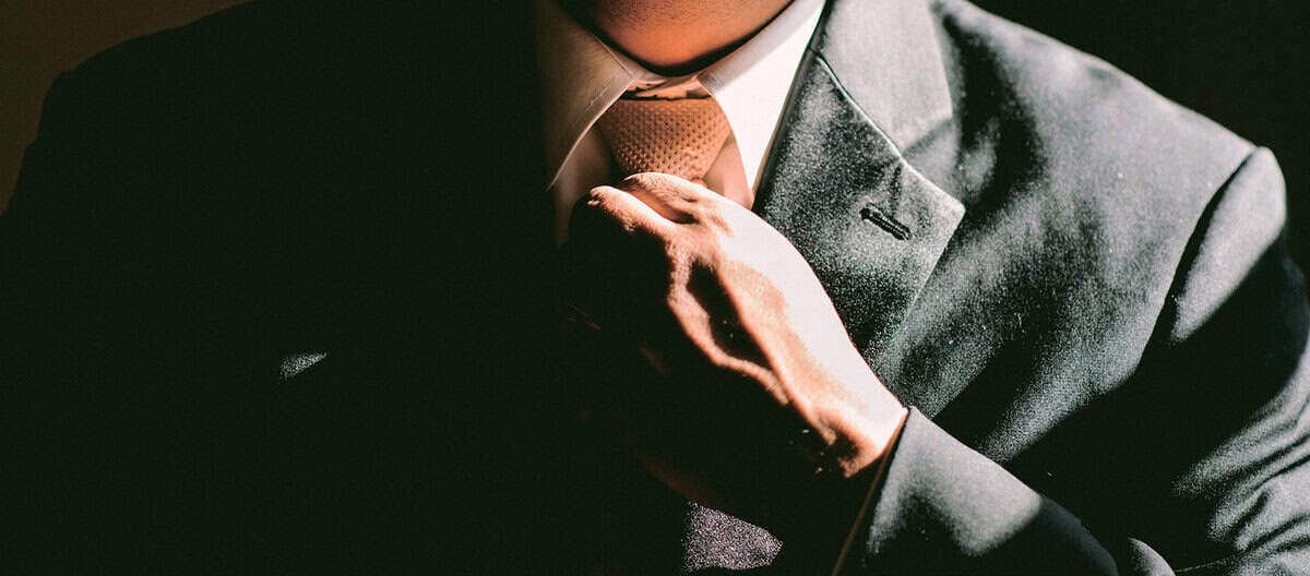 Харанхуй костюмтай хүн цайвар өнгийн зангиагаа тааруулдаг. Энэхүү дүр зураг гайхалтай гэрэлтэж, хүчтэй сүүдэр гар, зангиа, костюмны хэсгийг онцлон харуулсан нь шинэ сорилтуудыг даван туулахад бэлэн бизнес эрхэлдэг хүний мөн чанарыг сэргээдэг. Зурган дээр хүний царай харагдахгүй байна. - Business.MN