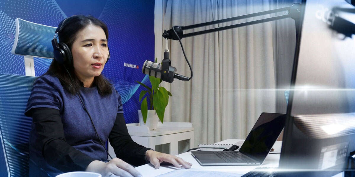 Ширээний ард чихэвч зүүгээд микрофоноор ярьж байгаа эмэгтэй, энтрепренер гэдэг нь тодорхой. Түүний өмнө зөөврийн компьютер, бичиг баримт байгаа. Энэхүү тохиргоо нь мэргэжлийн тоног төхөөрөмж, дижитал хээтэй цэнхэр дэвсгэр бүхий дуу бичлэгийн студи эсвэл оффис бололтой. - Business.MN