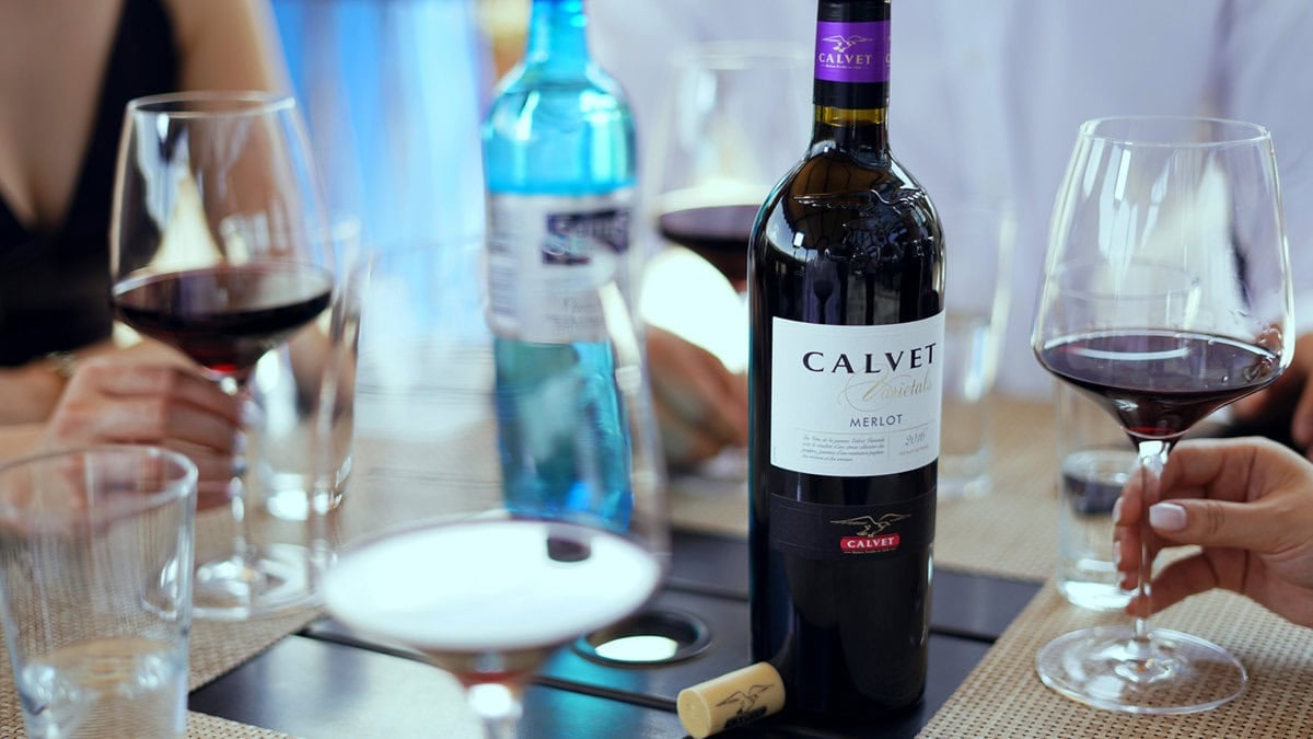 Голд нь нэг шил Calvet Merlot дарс тавьсан ширээ тойрон сууж буй хэсэг хүмүүс. Тэд улаан дарсаар дүүргэсэн хундага барьдаг. Ширээнд шил, усны сав, үйсэн байна. Уур амьсгал нь энгийн бөгөөд тайван байдаг. - Business.MN