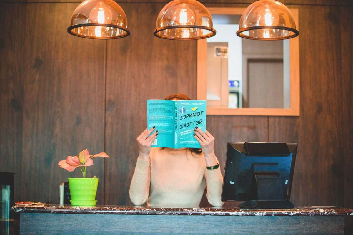 Бизнес энтрепренер лангууны ард зогсоод цэнхэр ном уншиж, дээр нь гурван унжлагатай гэрэл, хажууд нь ногоон ургамал байдаг. - Business.MN