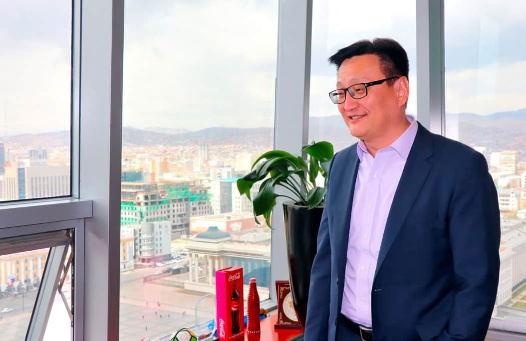 Костюм, нүдний шил зүүсэн бизнес энтрепренер цаадах нь хотын өнгө үзэмжтэй цонхны дэргэд зогсож байна. - Business.MN