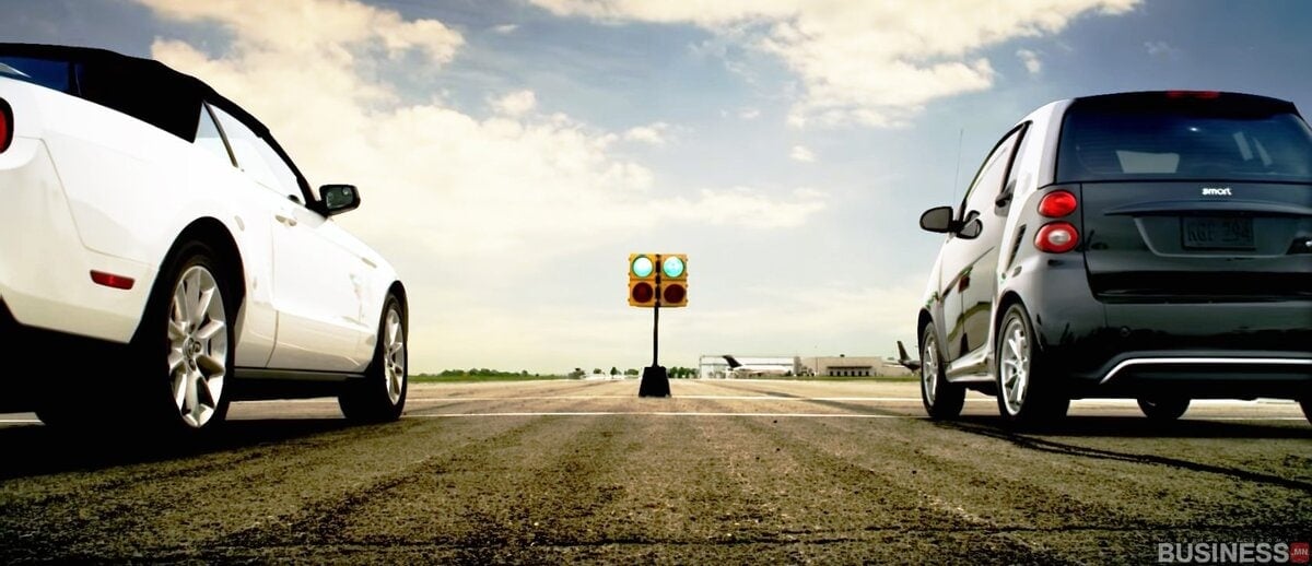 Драг уралдааны гарааны шугамд цагаан хөрвөх машин, хар авсаархан машин эгнэн зогсох бөгөөд тэдний хооронд гэрлийн мод бардам зогсож байна. Жолооч нар бол зоригтой энтрепренер бөгөөд дугуйгаа шийдэмгий шүүрч авдаг. - Business.MN