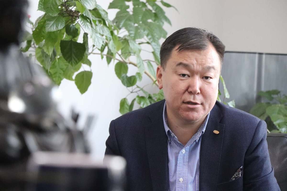 Бараан пиджак, цэнхэр алаг цамц өмссөн, энтрепренер байж магадгүй эрэгтэй, цаана нь ногоон навчит ургамлуудтай гэрт сууж байна. - Business.MN