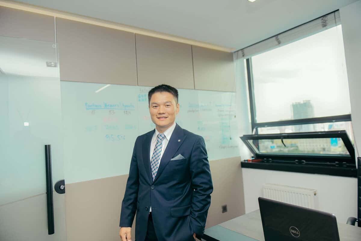 Ажил хэрэгч хувцастай эр оффисын өрөөнд инээж зогсохдоо самбар, цонхны ард зогсож, компанийхаа бизнесийг ирээдүйд чиглүүлж буй энтрепренерийн хувьд итгэл, амжилтыг цацруулж байна. - Business.MN