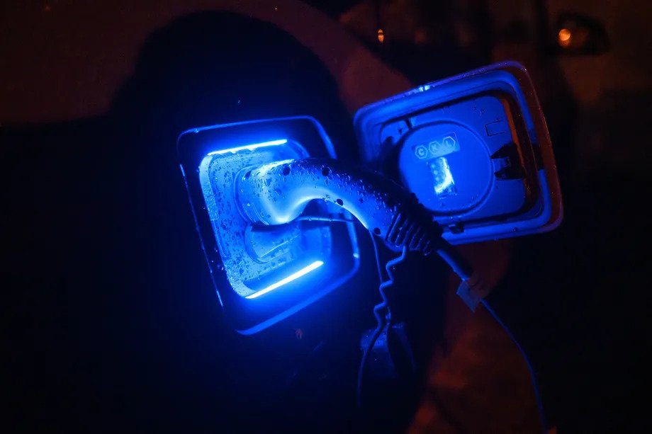 Манай компанийн ногоон санаачилгад чухал ач холбогдолтой цахилгаан тээврийн хэрэгслийг шөнийн цагаар цэнэглэж байна. Цэнхэр LED гэрлээр гэрэлтдэг цэнэглэх порт нь тээврийн хэрэгсэлд холбогдсон кабелийг харуулж байна. Кабель болон порт дээр усны дусал харагдаж байгаа нь нойтон цаг агаарын нөхцөл байдлыг илтгэнэ. - Business.MN