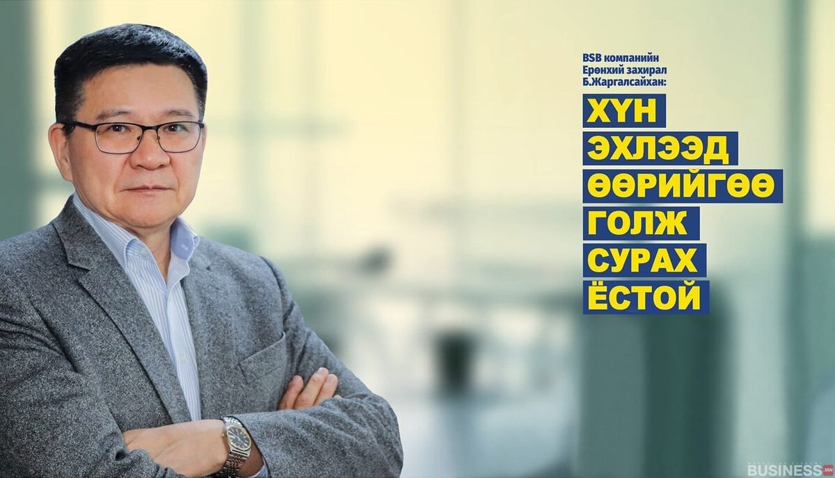 Нүдний шил, костюм өмссөн эрэгтэй гараа зөрүүлэн зогсож, оффисын бүдгэрсэн дэвсгэр дээр Монгол компани гэсэн бичвэрийн хажууд өөртөө итгэлтэй байна. - Business.MN