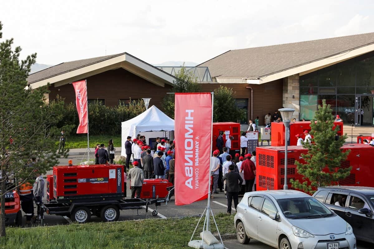 Хэд хэдэн улаан өнгийн тоног төхөөрөмж, цагаан майхан дор ярилцаж буй хэсэг энтрепренер, гадаа цугларсан олон оролцогчдыг харуулсан гадаа арга хэмжээ. Цагаан бичээстэй улаан тугнууд байгаа бөгөөд ойролцоо зогсоолтой машинууд байдаг. Цаана нь том барилга харагдана. - Business.MN