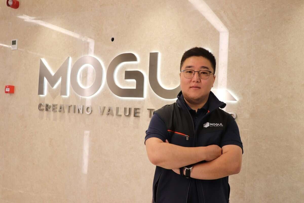 Богино хар үстэй, нүдний шил зүүсэн, хар хөх өнгийн цамц, хар хантааз өмссөн эрэгтэй "МОГУЛ" гэсэн гэрэлт үсэгтэй, "ҮНЭ ЦЭВЭРЛЭХЭЭР" гэсэн бичээстэй хананы өмнө гараа зөрүүлэн зогсож байна. Энэхүү энтрепренер нь түүний компаний инновацид тууштай ханддагийг тодорхой харуулж байна. - Business.MN