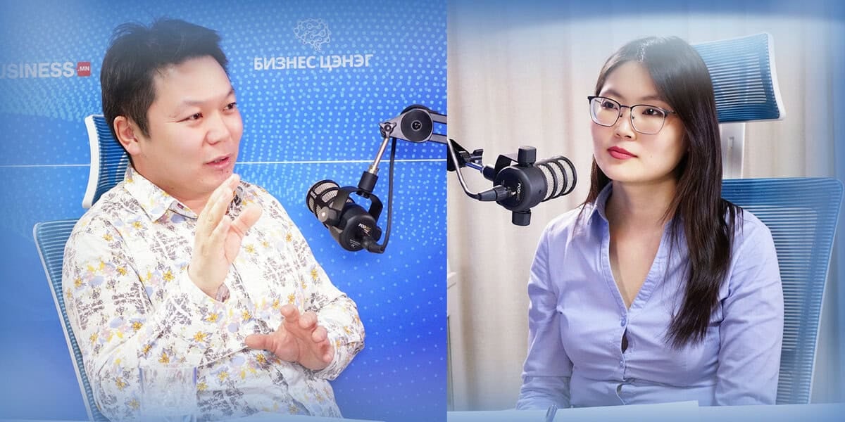 Хэлэлцүүлэгт оролцож буй хоёр хүн тус бүр микрофоноор ярьж, цэнхэр дэвсгэр дээр бизнесийн тухай бичвэр бичжээ. - Business.MN