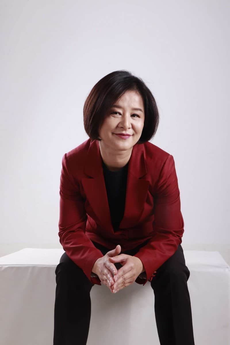 Улаан пиджак өмссөн богино үстэй эмэгтэй цагаан гадаргуу дээр суугаад гараа атгасан итгэлтэйгээр инээмсэглэж байгаа нь амжилттай энтрепренерийн сүнсийг илэрхийлдэг. - Business.MN