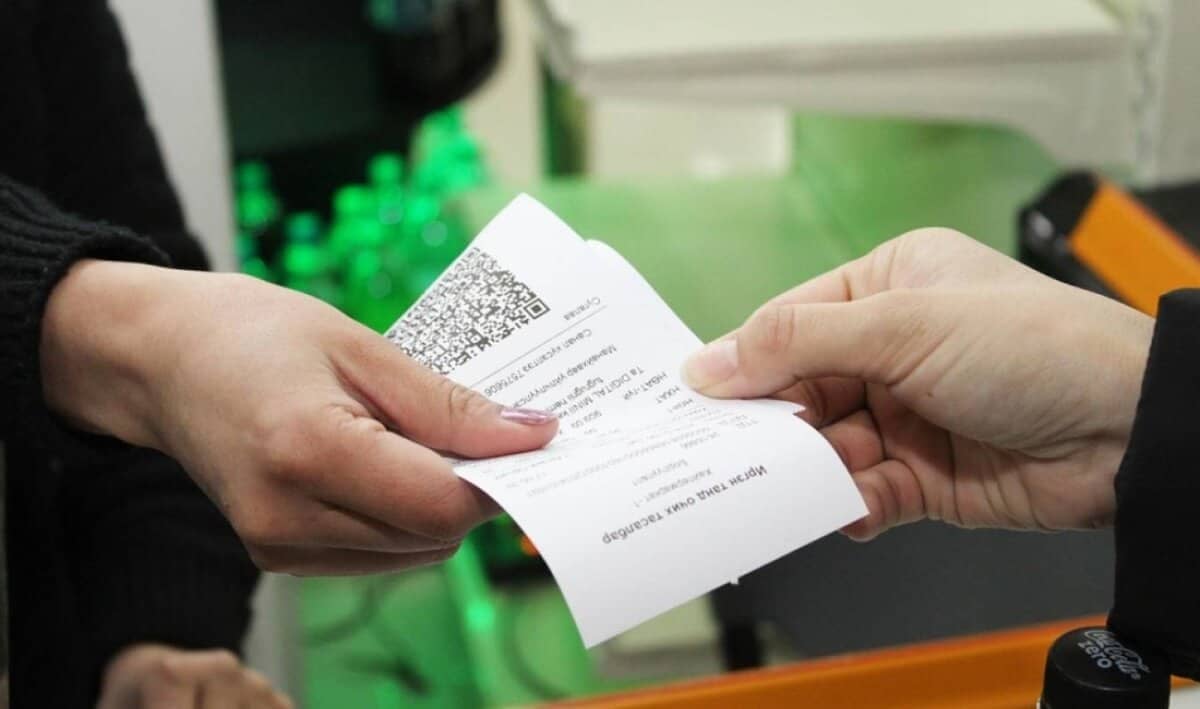 Баримт солилцож буй хоёр гарыг ойроос харах нь жижиг бизнесийн гүйлгээний агшин зураг. Хар өнгийн ханцуйтай нэг гар нь QR код агуулсан хэвлэмэл баримтыг цайвар өнгийн арьстай нөгөө гартаа өгч байна. Ар талд нь ногоон шингэнтэй шилнүүд харагдах бөгөөд энэ нь энтрепренерийн өдөр тутмын агшныг дүрслэн харуулах болно. - Business.MN