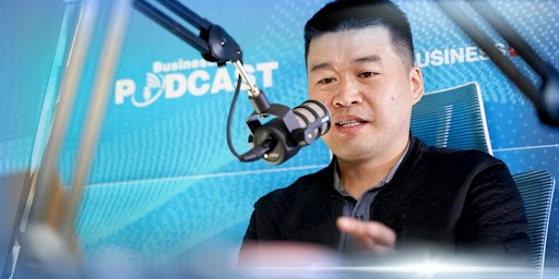 Нэг хүн дуу бичлэгийн студид суугаад микрофоноор ярьж байна. Түүний ард байгаа том самбар дээр "Бизнес Подкаст" гэж бичсэн нь хөтөлбөрийн мөн чанарыг илтгэнэ. Энтрепренерийн хувьд тэрээр хамгийн сүүлийн үеийн компаний ажил үйлсийнхээ талаар ярихдаа нэг гараараа дохиж, сүй тавьсан бололтой. - Business.MN