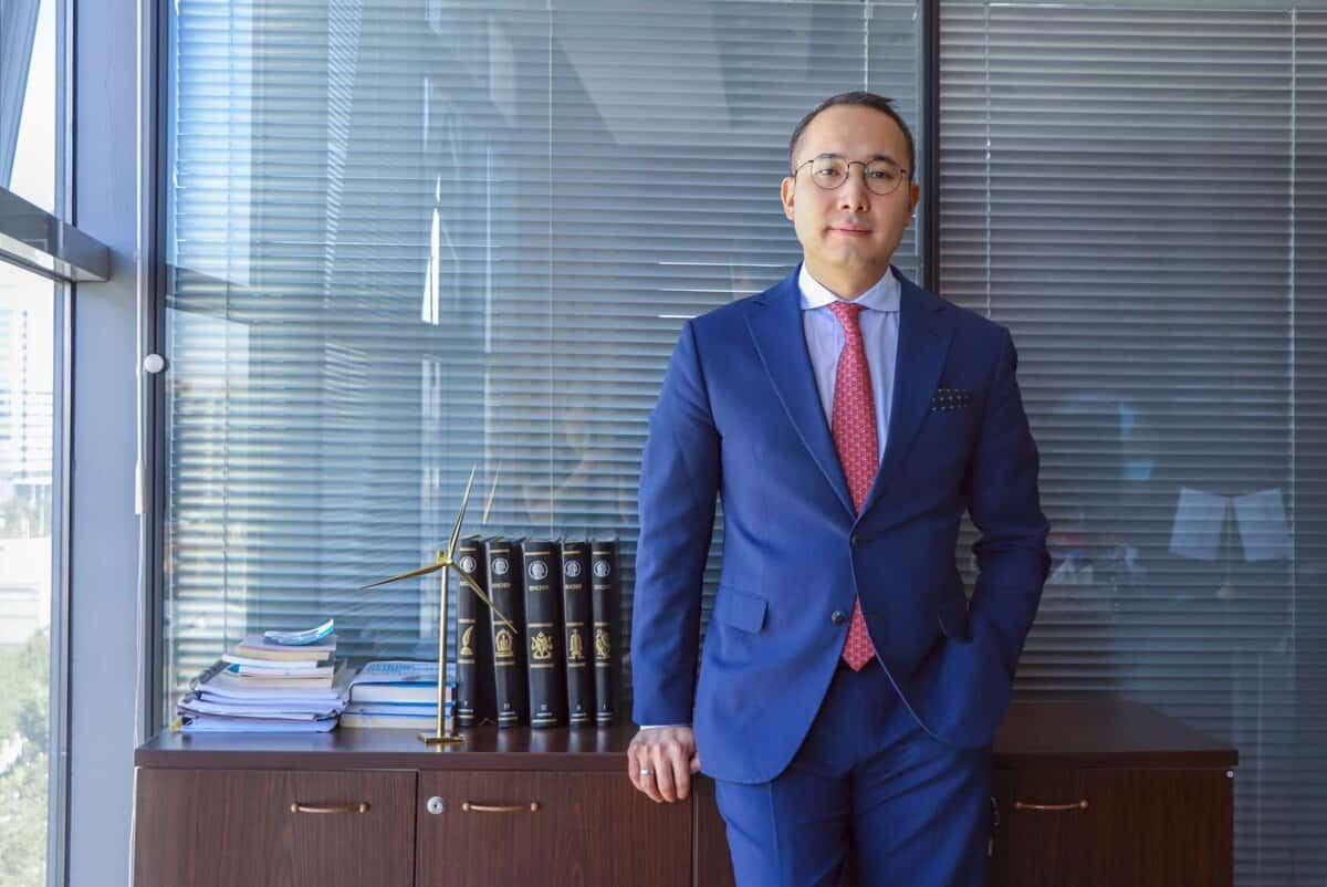 Цэнхэр костюмтай улаан зангиа зүүсэн бизнес эрхлэгч оффисын цонхны дэргэд зогсож, компанийнхаа хамгийн сүүлийн үеийн бизнесүүдийн ном, цаасаар дүүрэн шүүгээг налан зогсож байна. - Business.MN