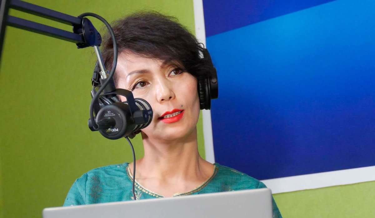 Чихэвч зүүсэн бизнес эрхлэгч цэнхэр дэвсгэртэй зөөврийн компьютерын өмнө суугаад микрофоноор ярьж байна. - Business.MN