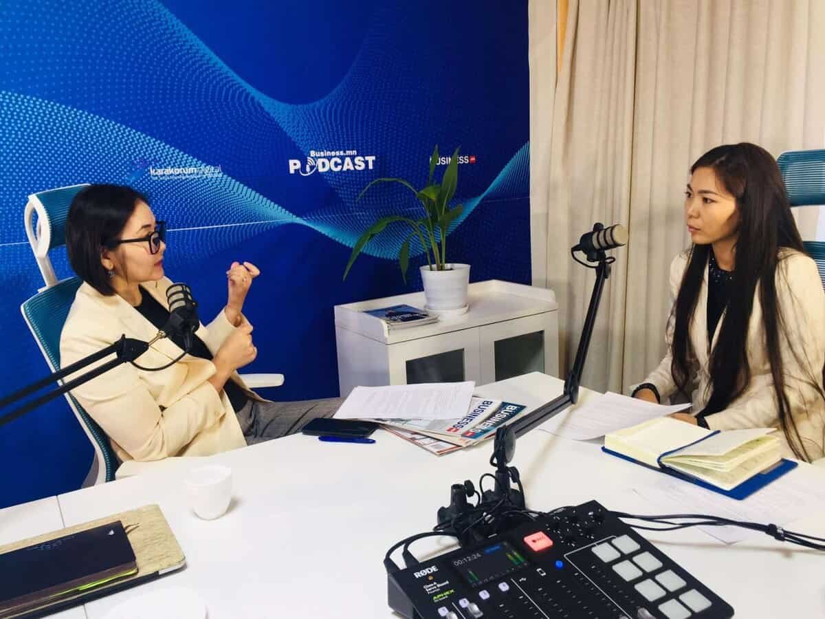 Хоёр эмэгтэй, нэг нь энтрепренер, подкаст дээр ярилцлага өгч, ширээн дээр микрофон, тэмдэглэл хөтлөн бие биенийхээ өөдөөс харж суугаад бизнесийн туршлагаасаа ярилцаж, компанийг удирдах тухай ойлголтоо хуваалцаж байна. - Business.MN
