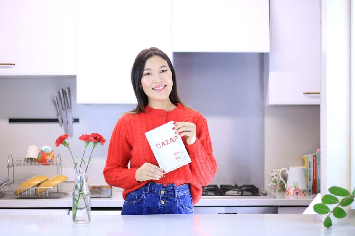 Улаан ноосон цамц, цэнхэр жинсэн өмд өмссөн эмэгтэй "Самар" нэртэй ном барин инээмсэглэж байна. Тэр лангуун дээр улаан цэцэгтэй ваар, ард нь аяга тавагны тавиур, тавиур дээр янз бүрийн ажил хэргийн зүйл тавьсан гэрэлтэй гал тогооны өрөөнд зогсож байгаа нь түүний бизнес эрхлэх сэтгэлийг илтгэнэ. - Business.MN