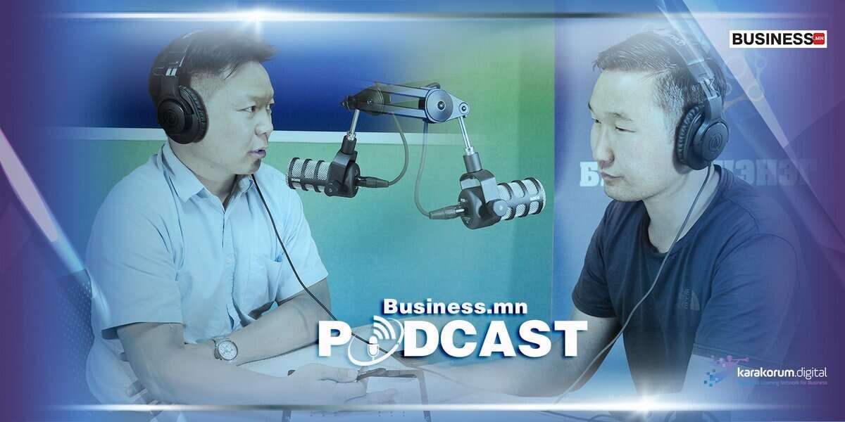 Подкаст студид микрофоноор ярьж буй хоёр эр бие биенийхээ өөд өөдөөсөө харан сууж байна. Арын дэвсгэр дээр "Business.mn Podcast" гэсэн бичвэр бүхий тод өнгийг харуулдаг. Энэ тохиргоо нь мэргэжлийн бичлэг хийх орчинг санал болгож байна. - Business.MN