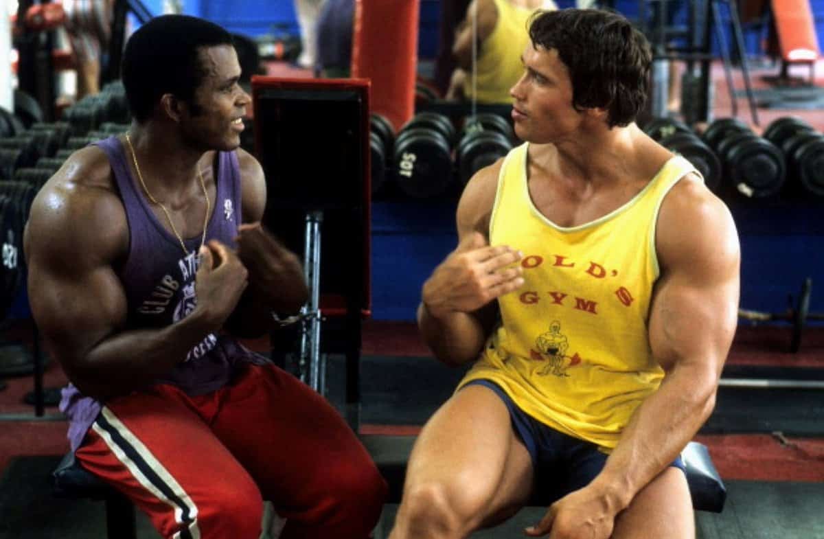 Биеийн тамирын хувцас өмссөн булчинлаг хоёр эрэгтэй вандан сандал дээр суугаад бизнесийн стратегийн талаар ярьж байна. Тэдний ард хүндийн өргөлтийн тоног төхөөрөмж нь фитнесс ба бизнес эрхлэх өвөрмөц хослолыг бий болгодог. - Business.MN