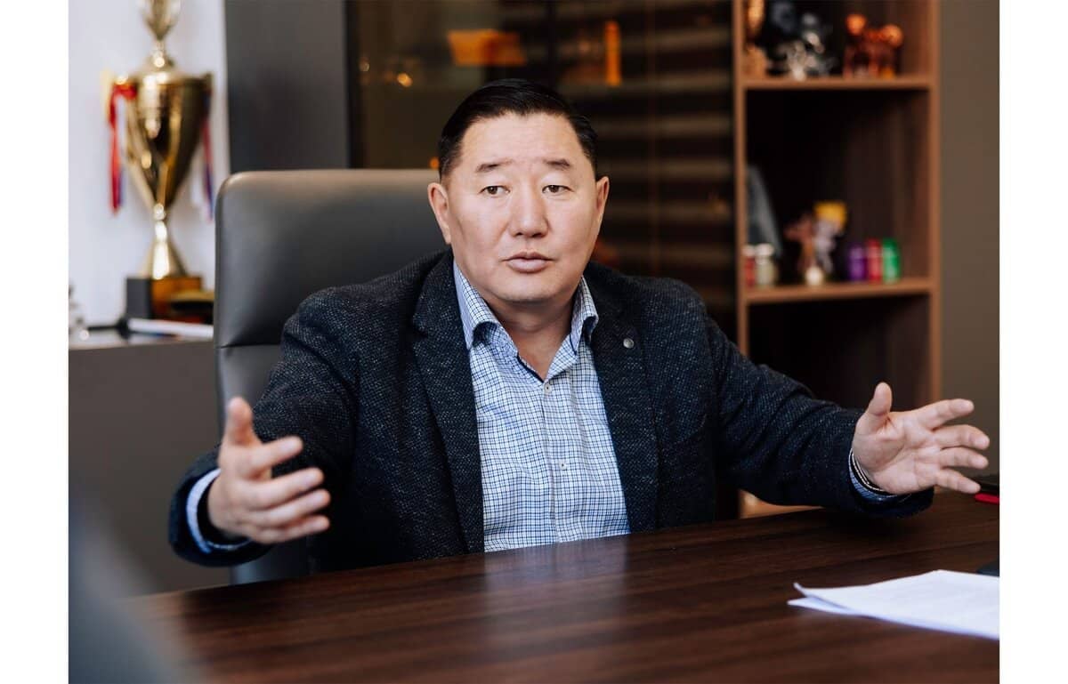 Нэг эр ширээнийхээ ард суугаад гараараа дохиж, нухацтай царайлна. Тэр энтрепренерийн анхаарлыг татсан цамцан дээр бараан өнгийн пиджак өмссөн байна. Арын дэвсгэр дээр том цом, төрөл бүрийн эд зүйлс бүхий тавиурууд, цонхтой. Түүний урд талын ширээн дээр бизнесийн шийдвэрийг харуулсан баримт бичиг байдаг. - Business.MN