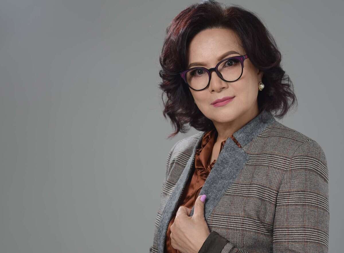 Нүдний шилтэй, дөрвөлжин пиджак, бор цамц өмссөн бизнес эрхлэгч саарал дэвсгэр дээр зогсож, камер руу харж байна. - Business.MN