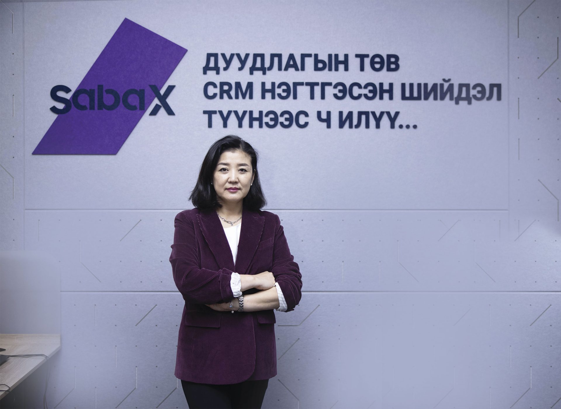 Мөр хүртлээ урт хар үстэй, бургунд пиджак өмссөн эмэгтэй "Сабакс" компанийн лого, монгол бичвэр бүхий хананы өмнө гараа зөрүүлэн зогсож байна. Арын дэвсгэр нь оффисын орчин байсан бололтой, өөрийн бизнест гүнээ шингэсэн өөртөө итгэлтэй энтрепренерийг дүрсэлсэн байна. - Business.MN