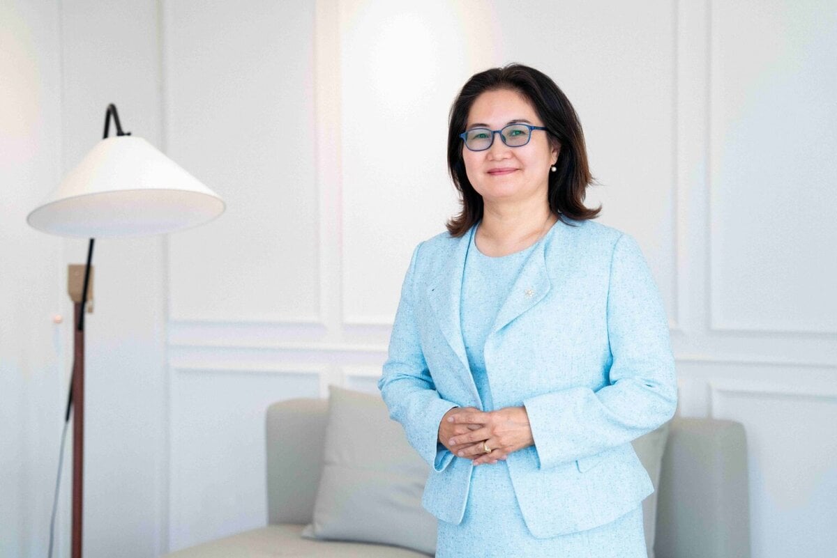 Мөр хүртлээ хар үстэй, нүдний шил зүүсэн, цайвар цэнхэр өнгийн костюм өмссөн эмэгтэй гараа атгасан байдалтай инээмсэглэн зогсох нь цагаан хана, шалны гэрэл, буйдан бүхий гэрэлт, орчин үеийн өрөөнд бахархал босс мэт харагдаж байна. - Business.MN