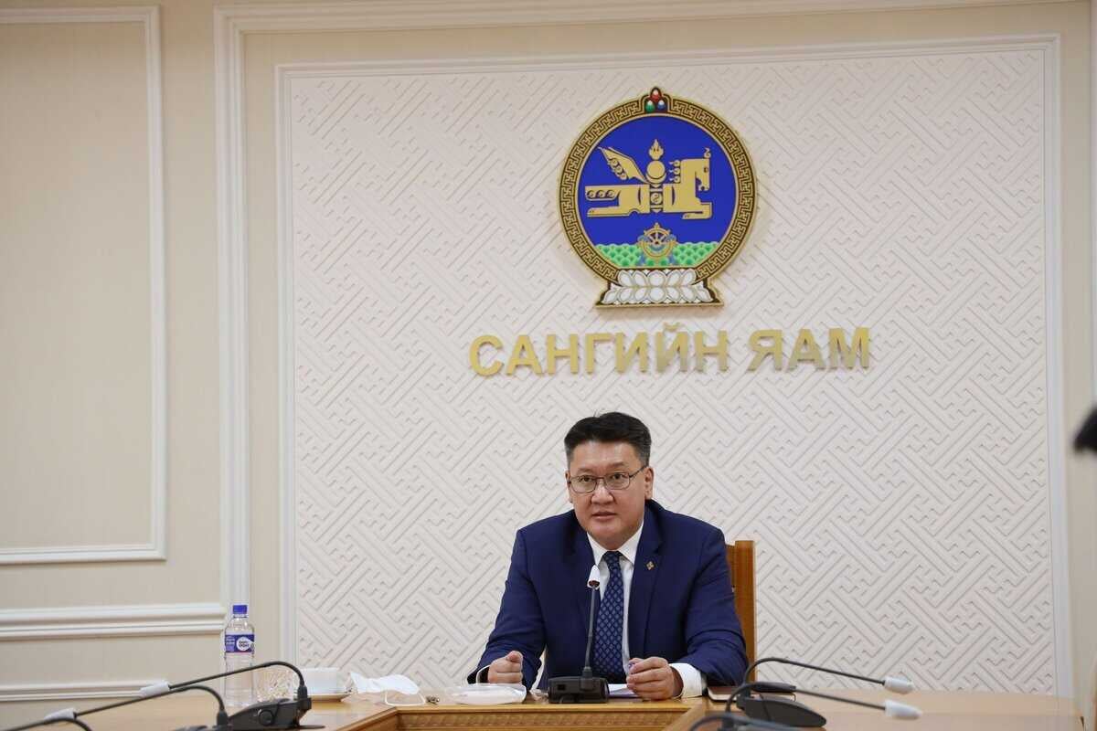 Цэнхэр костюмтай хүн урд нь микрофонтой ширээний ард сууж байна. Сүлд тэмдэг, алтан бичээс бүхий хананы өмнө байрлуулсан тэрээр бизнестэй холбоотой асуудлыг хөндөж байгаа бололтой. Ширээн дээр усны сав, цаас зэрэг янз бүрийн эд зүйлс байгаа нь засгийн газрын албан ёсны уур амьсгалыг сайжруулж байна. - Business.MN