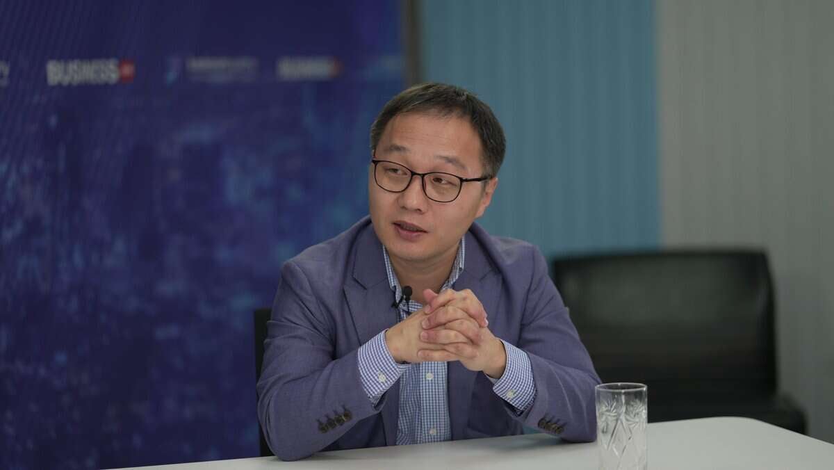 Нүдний шил, цэнхэр пиджак өмссөн хүн урд нь тунгалаг шилтэй ширээний ард сууна. Тэд гараа урдаа бариад ярьж байгаа бололтой. Арын дэвсгэр нь бизнестэй холбоотой график, текст бүхий цэнхэр ханатай. - Business.MN